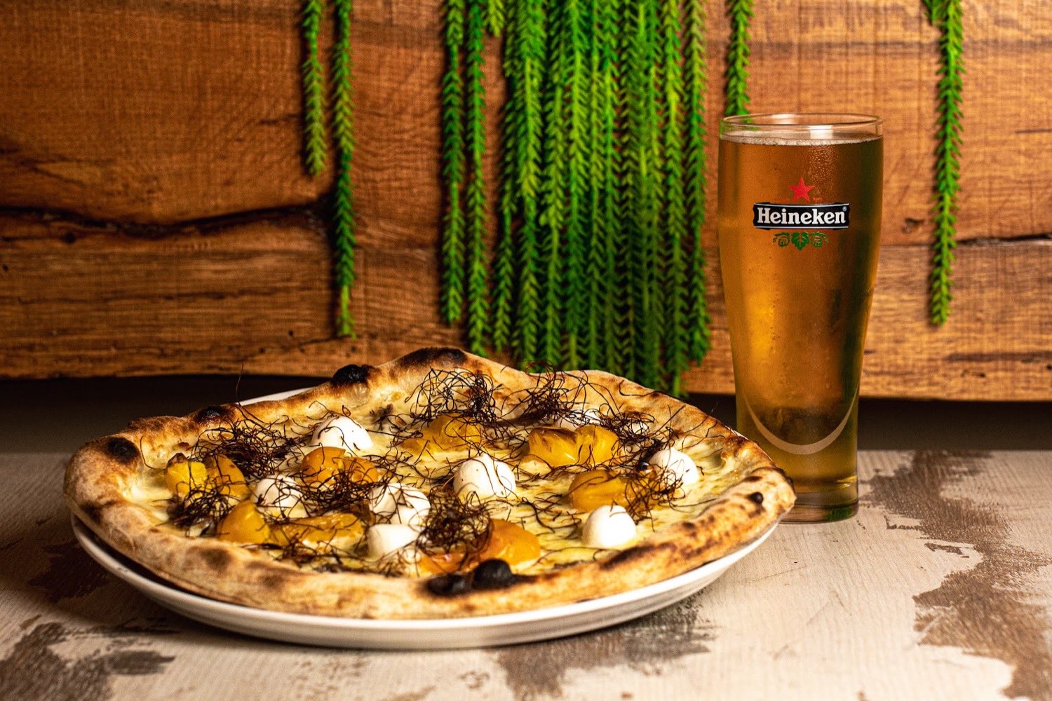 Pizza gourmet con datterini gialli, mozzarella e cipolla croccante, servita con una birra